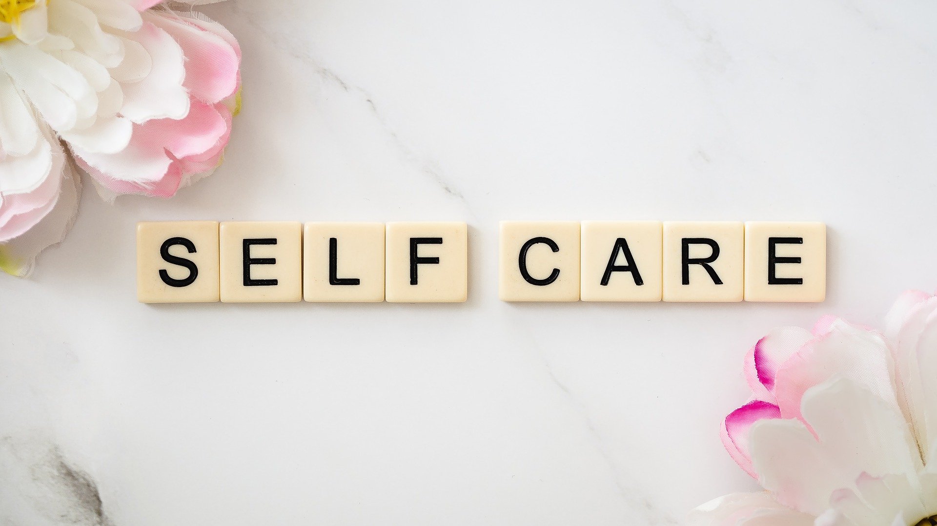 scrabble tiles spelling out self-care, with 2 flower blooms